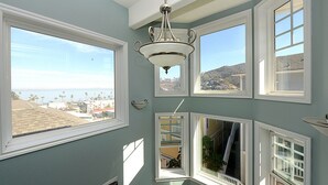 A room with a large bay window, a ceiling fan, and a view of a coastal landscape. - 217BA: Lovely 3 bdrm, 2.5 Bath, Ocean Views, Wifi (Avalon)