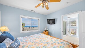 A bedroom with a bed, a ceiling fan, a TV, a window with a view, and a door leading to a balcony. - 217BA: Lovely 3 bdrm, 2.5 Bath, Ocean Views, Wifi (Avalon)