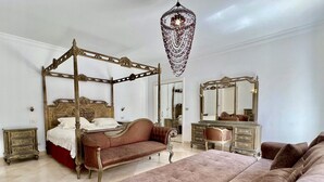 Een luxueuze slaapkamer met een hemelbed, een chaise longue, een grote spiegel en een kroonluchter.