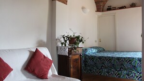 Habitació amb un sofà blanc, un llit amb roba de llit estampada, una planta en test i una arcada de maó.