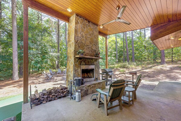 An outdoor patio with a stone fireplace, seating area, and a grill.