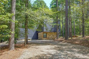 A cabin surrounded by tall trees with a gravel driveway leading to the entrance.