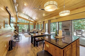 A spacious room with a large wooden ceiling, a central island with a bar area, and a stone fireplace. - Hot Tub, Fire Pit, Forest Views! Broken Bow Cabin (Broken Bow)