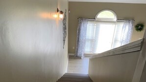 A wooden staircase leading to a landing with a view of a window with curtains. - Cozy, Stylish Garden Home (Dothan)
