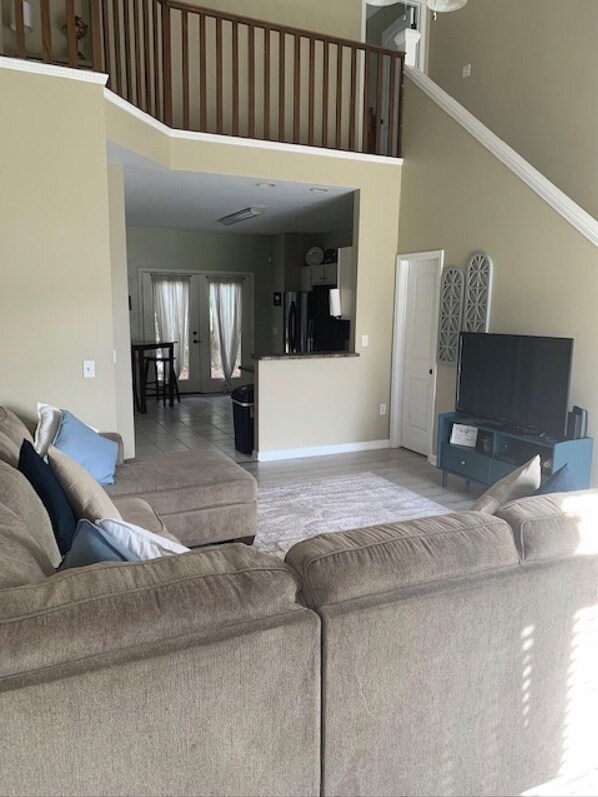 A spacious living room with a large sectional sofa, a flat-screen TV, and a staircase leading to an upper level. - Cozy, Stylish Garden Home (Dothan)