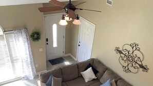 A spacious living area with a large L-shaped sectional sofa, a ceiling fan, and a decorative wall piece. - Cozy, Stylish Garden Home (Dothan)