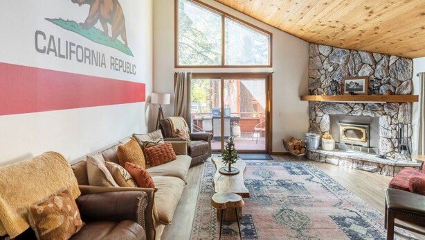 Ein gemütliches Wohnzimmer mit Kamin aus Stein, einem großen Fenster und einem Bären-Logo an der Wand.