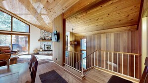 Ein geräumiger Wohnbereich mit Kamin aus Stein, Holzboden und einer Treppe mit Geländer.