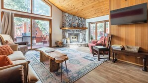 Ein gemütliches Wohnzimmer mit Kamin aus Stein, Holzboden und großen Fenstern.