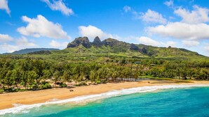A beach with clear turquoise waters, a sandy shore, and a mountain with rocky peaks in the background.