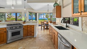 A modern kitchen with a gas stove, oven, and dishwasher, wooden cabinets, and large windows offering a view of the ocean.