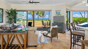 A spacious living room with a large TV, comfortable seating, and a view of the ocean.