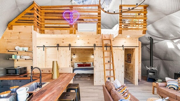 Een gezellig houten huisje van binnen met een slaapkamer op de entresol, een eethoek en een keuken.