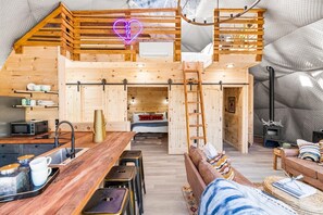 A cozy cabin interior with a loft bedroom, a dining area, and a kitchen.