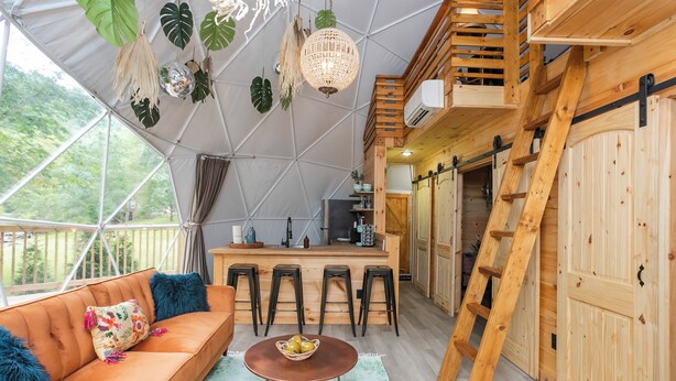 A cozy, well-lit tent with a sofa, a dining table, and bar stools. - ✨🥂 Glamping Dome with Full Bath, Kitchen, Fire Pit, & Grill (Cosby)