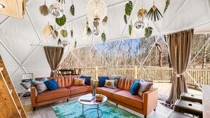 A cozy tented room with a sectional sofa, a small table, and hanging plants. - ✨🥂 Glamping Dome with Full Bath, Kitchen, Fire Pit, & Grill (Cosby)