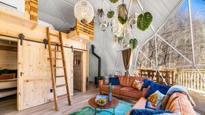 A cozy, well-lit interior with a wooden ladder, a sofa with colorful cushions, and a dining table with a bowl of fruit. - ✨🥂 Glamping Dome with Full Bath, Kitchen, Fire Pit, & Grill (Cosby)