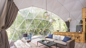 Un espace de vie spacieux et moderne, doté d’une grande fenêtre, d’un ensemble de canapés, d’une table basse et d’un buffet en bois.
