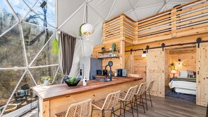 Un espace de vie moderne et décloisonné, comprenant un coin bar en bois, des sièges et une cuisine.
