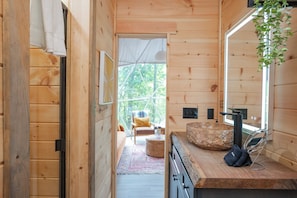 Relax in a cozy cabin with a large window offering a view of the outdoors, a seating area, and a self-service bathroom with sink and mirror.