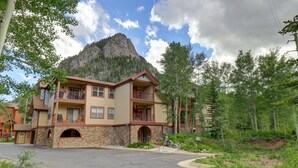 A multi-story building with a stone facade, balconies, and a mountain backdrop. - 101 Streamside Lane 2 Bedroom Condo by RedAwning (Frisco)