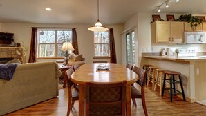 A cozy living room with a wooden dining table, a sofa, and a fireplace. There is a kitchen area with a microwave and cabinets. - 101 Streamside Lane 2 Bedroom Condo by RedAwning (Frisco)