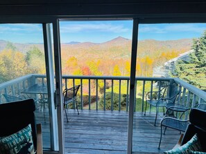 Una terraza de madera con mobiliario exterior y vistas al follaje otoñal y montañas.