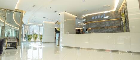 A modern hotel lobby with a reception desk, glass walls, and potted plants.