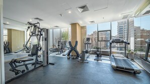 Un gimnasio moderno con diversos equipos de ejercicio, ventanas amplias y vistas a la ciudad.