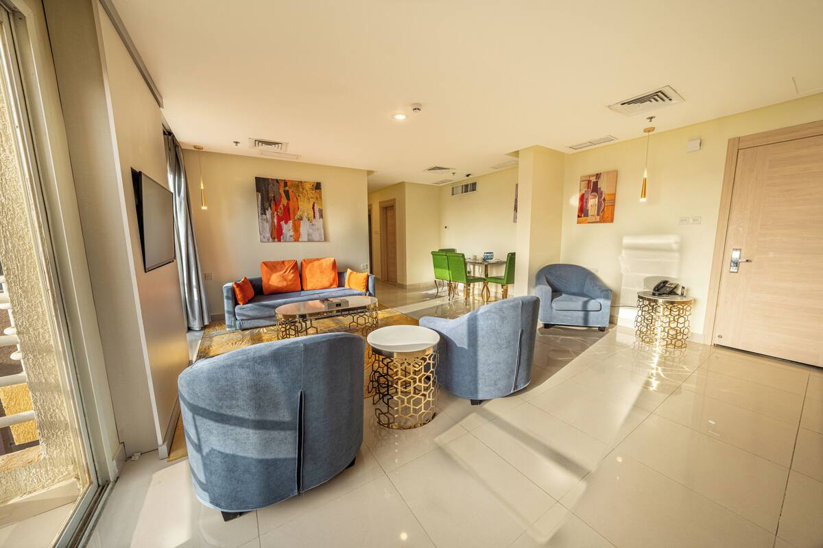 Una sala de estar moderna con un sofá, sillones y una mesa de centro. Hay una zona de comedor con sillas verdes y una mesa.