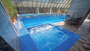 Una piscina interior con hidromasaje, rodeada por un cerramiento de vidrio y suelo de baldosas.