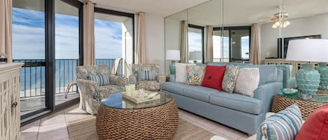 A spacious living room with a large sofa, a round coffee table, and a balcony with a view of the ocean.
