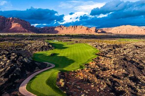 A golf course with a winding path, surrounded by rocky terrain and mountains.
