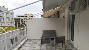 A balcony with a table and chairs, a metal railing, and a view of buildings in the background.