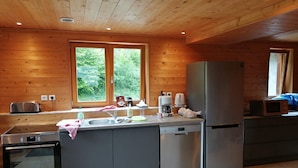Una cocina compacta con paredes de madera, horno empotrado, lavavajillas y refrigerador.