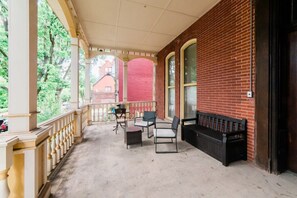 A covered porch with a brick wall, a bench, and outdoor furniture. - Comfort Suite - Walkable - GroupStay (Pittsburgh)