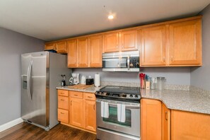 A kitchen with wooden cabinets, a stainless steel refrigerator, a microwave, and an oven. - Comfort Suite - Walkable - GroupStay (Pittsburgh)