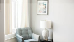 A room with a window, a framed picture on the wall, a lamp on a side table, and a chair. - Parking - Walkable - GroupStays - Washer (Pittsburgh)