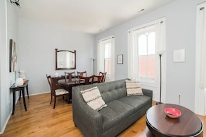 A living room with a gray sofa, wooden dining table, chairs, and a round coffee table. - Parking - Walkable - GroupStays - Washer (Pittsburgh)