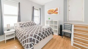 A bedroom with a bed, bedside table, chair, and a wall-mounted shelf. - Parking - Walkable - GroupStays - Washer (Pittsburgh)
