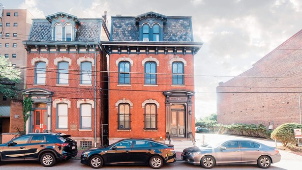 A two-story red brick building with a stone facade, a black car parked in front, and a clear sky. - Parking - Walkable - GroupStays - Washer (Pittsburgh)