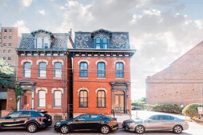 A two-story red brick building with a stone facade, a black car parked in front, and a clear sky.