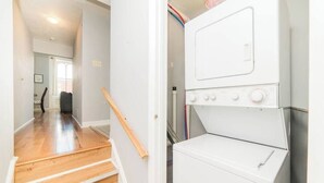 A laundry area with a washer and dryer, wooden stairs, and a hallway leading to a door. - Parking - Walkable - GroupStays - Washer (Pittsburgh)
