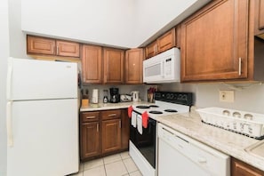 A kitchen with wooden cabinets, a white refrigerator, a microwave, a stove, and a dishwasher.