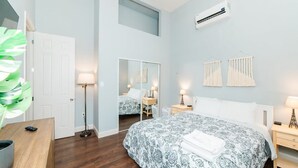 Un dormitorio con cama, mesitas de noche, un espejo y un equipo de aire acondicionado.