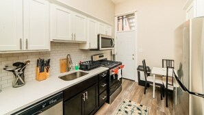 A kitchen with white cabinets, a microwave, a stove, a dishwasher, and a dining area with chairs and a table. - Studio Suite - No Steps - Walkable & Free Parking (Pittsburgh)
