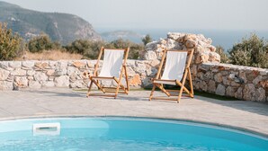 A poolside area with two wooden chairs and a stone wall. - Dione Villa 3: private pool - amazing sea view - traditional minimal stone villa (STOUPA)