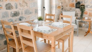 A wooden dining table set with white plates, silverware, and a small plant. The room features stone walls and a window with a view. - Dione Villa 3: private pool - amazing sea view - traditional minimal stone villa (STOUPA)