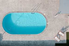 An aerial view of a rectangular swimming pool with a diving board, surrounded by tiled flooring.
