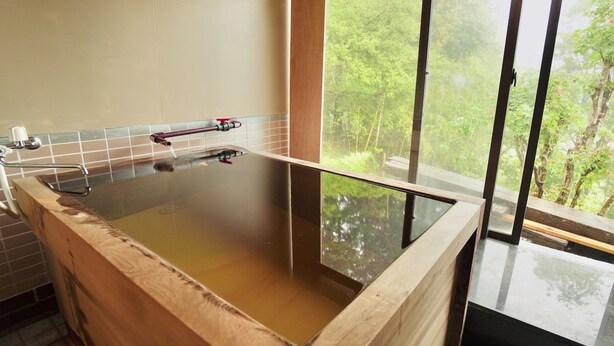 A wooden bathtub with a glass bottom, a faucet, and a window with a view of greenery. - Hakone Rose Hill Private Duplex Villa (Hakone)